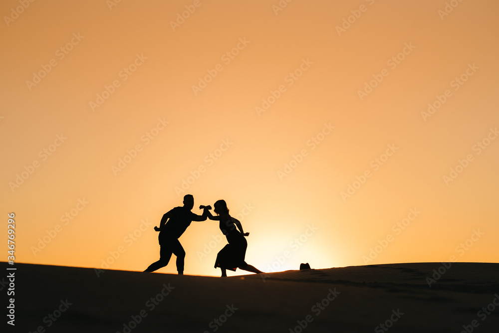 silhouettes of a happy young couple on a background of orange sunset in the sand desert