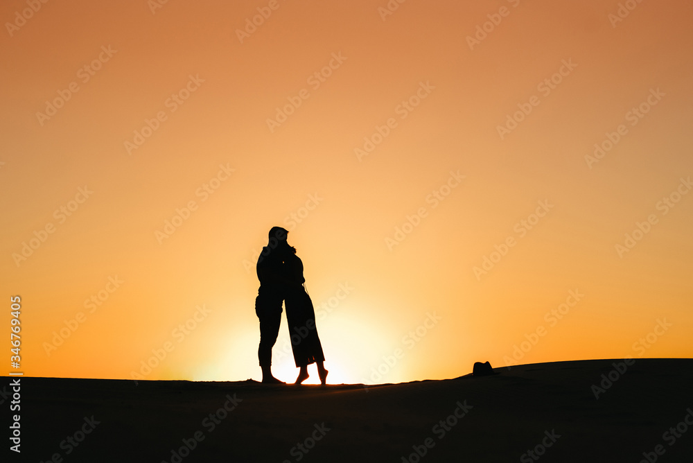 silhouettes of a happy young couple on a background of orange sunset in the sand desert