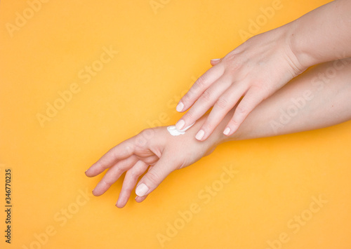 One hand smears the other hand with cream. Moisturizing cream, skin care cosmetics. Yellow background.
