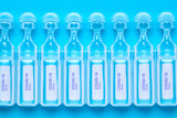 Coronavirus treatment concept. Close-up of  of ampoules with vaccine COVID-19 flat layed on a blue background. Global pandemic outbreak and healing the deadly coronavirus. Macro photograph.