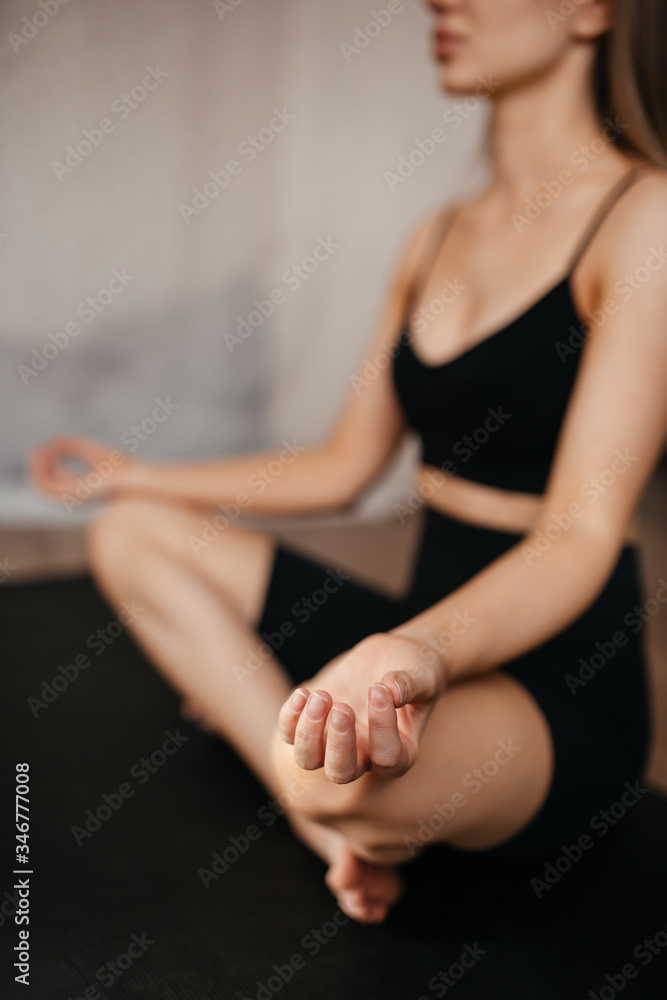 Fototapeta premium close-up shot of a beautiful girl who meditates at home sitting on a black rug in black clothes