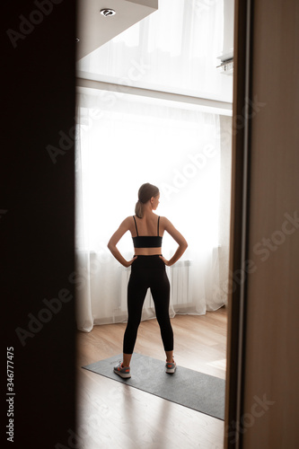 Beautiful girl at home in black sportswear is training on a black rug