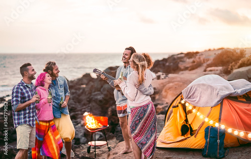 Group happy friends having fun camping outdoor - Young people drinking beers and playing guitar in campsite next the beach - Youth culture and travel vacation concept