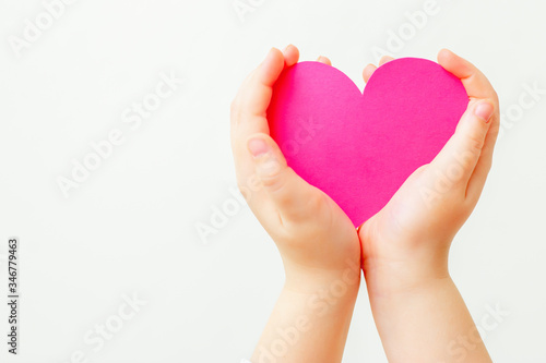 Closeup of child s hands holding paper pink heart on white background. Concept of love.