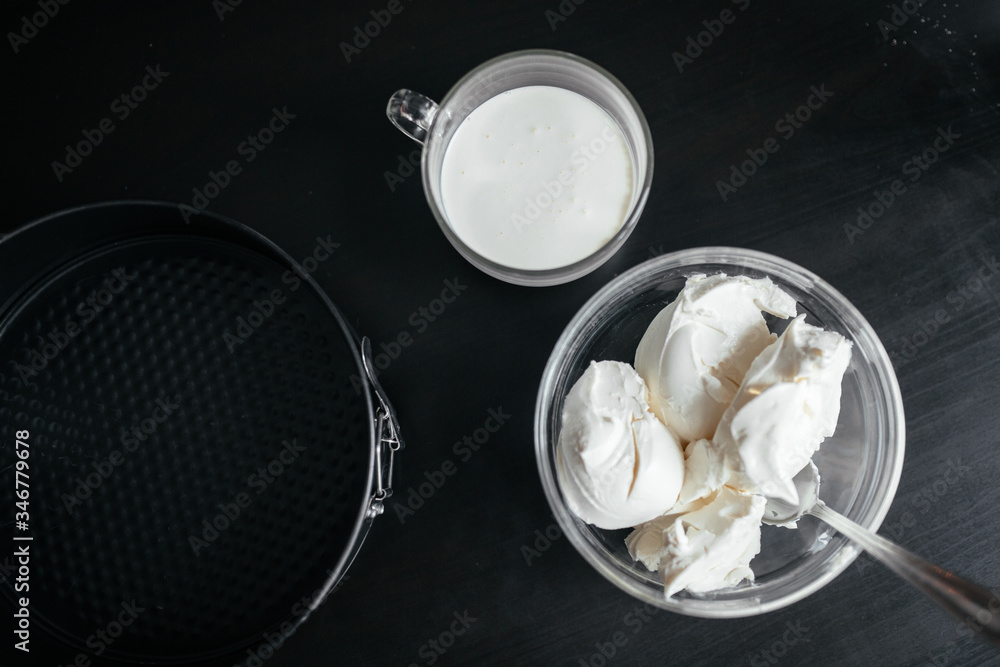 On a black table is a baking dish, cream and curd cheese in a cup On a black table is a baking dish, cream and curd cheese in a cup