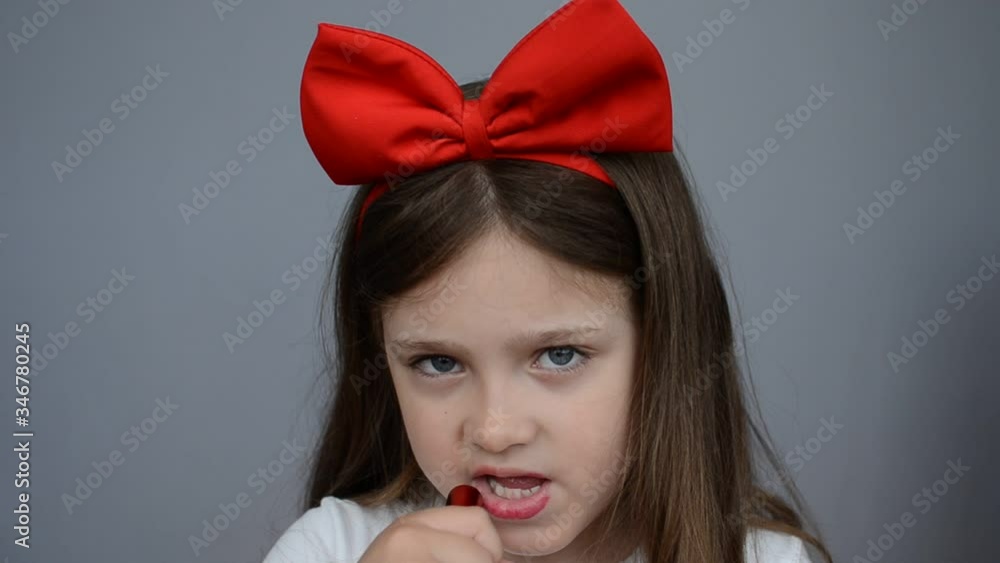 Little charming girl child with a big bow on her head paints her lips with lipstick Little charming girl child with a big bow on her head paints her lips with lipstick