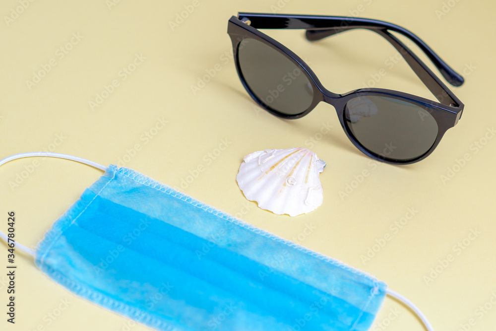 Closeup of medical face mask, sunglasses, seashell on a yellow background. Summer concept during pandemic of coronavirus. Closeup of medical face mask, sunglasses, seashell on a yellow background. Summer concept during pandemic of coronavirus.