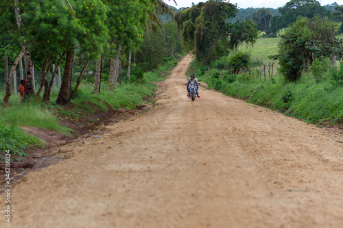 A man on a bike carrying a passenger and travelling on a dirt road in the bush © Hamidslens