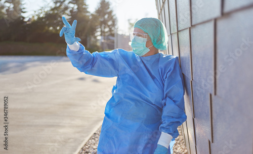 Arzt in Schutzkleidung zeigt Zahl Drei mit Fingern vor Klinik © Robert Kneschke