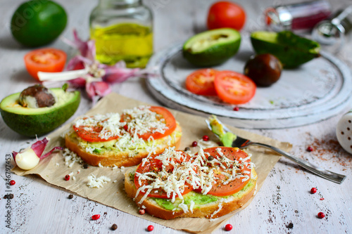 Two sandwiches with avocado, cheese and tomatoes, olive oil, garlic and spices in the background. Delicious and nutritious breakfast.