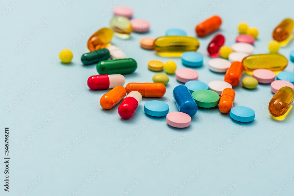 Selective focus of colorful pills and capsules on blue background