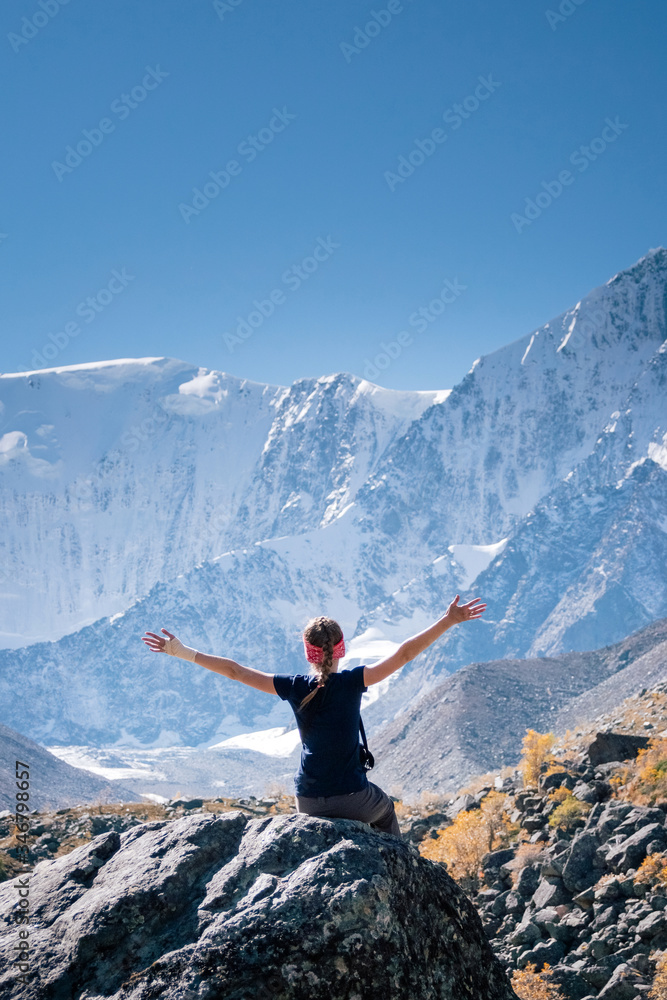 Happy young blonde woman in blue t-shirt sitting on a mountain top. Hiker relaxing on top of a mountain and enjoying sunny day.