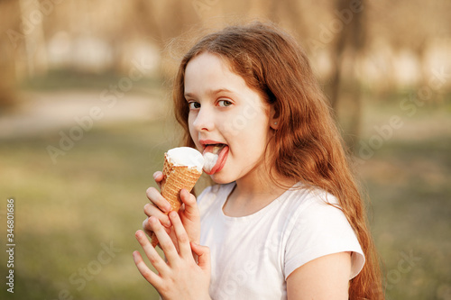 Curly girl eats ice cream in the summer park.