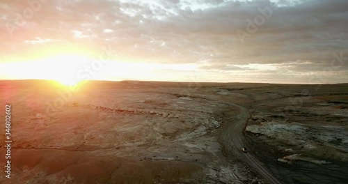 Aerial view Slow moving shot, Car moving on the rough road of Utah Badlands, Scenic view of Sun set in the background. photo