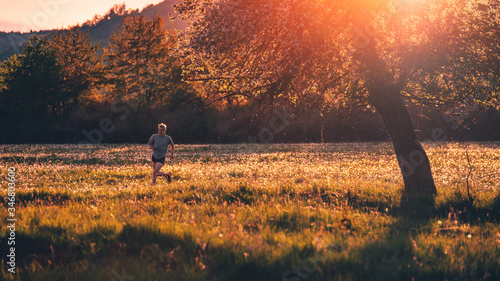 Male runner silhouette on spring meadow in orange sunset light