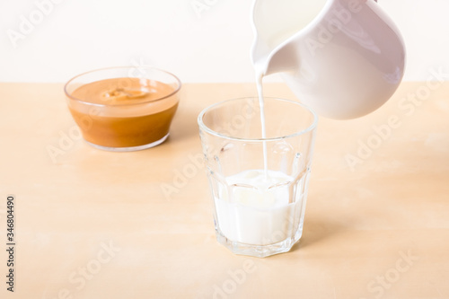 How to make coffee from dalgon. Step by step photo instruction. Step 5. Pour milk into a glass. Ingredients - instant coffee, sugar, water, milk and a whisk for whipping on a wooden background photo