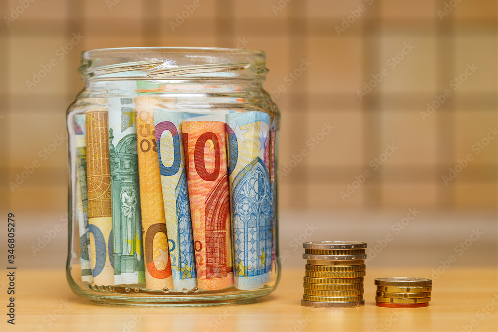 Euro banknotes in a glass jar, columns of coins close-up. The kitchen background is blurred. The concept of finance and economics. Euro banknotes in a glass jar, columns of coins close-up. The kitchen background is blurred. The concept of finance and economics.