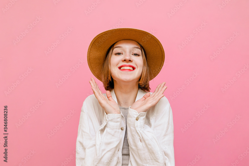 Portrait of joyful lady with happy face and clenched fists cheers, looks at camera and smiles. Cute girl in hat and light clothing rejoices on pastel pink background. Isolated. Portrait of joyful lady with happy face and clenched fists cheers, looks at camera and smiles. Cute girl in hat and light clothing rejoices on pastel pink background. Isolated.