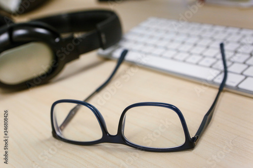 occhiali da vista su scrivania vicino alla tastiera di un computer e delle cuffie 