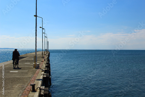 Seaside and concrete pier. Traditionally dressed man riding a bike on the pier.