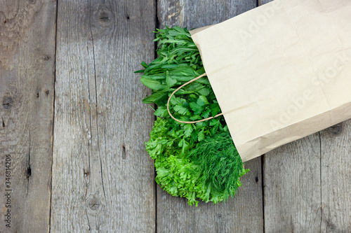 Fresh greens in a paper bag - green onions, dill, parsley, spinach, arugula, sorrel. Home delivery of food and fresh vegetables. Wooden background with place for text. Packaging and cooking.