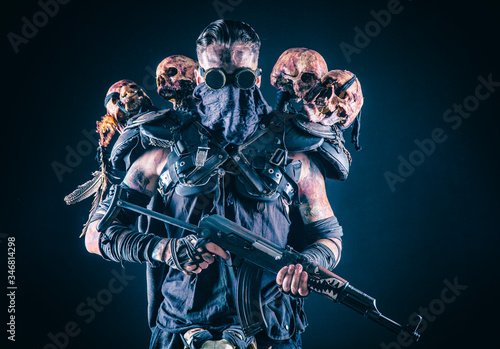 Post apocalyptic survivor, radioactive zone stalker, crazy serial killer or maniac in glasses and skulls on shoulders, with automatic rifle photo