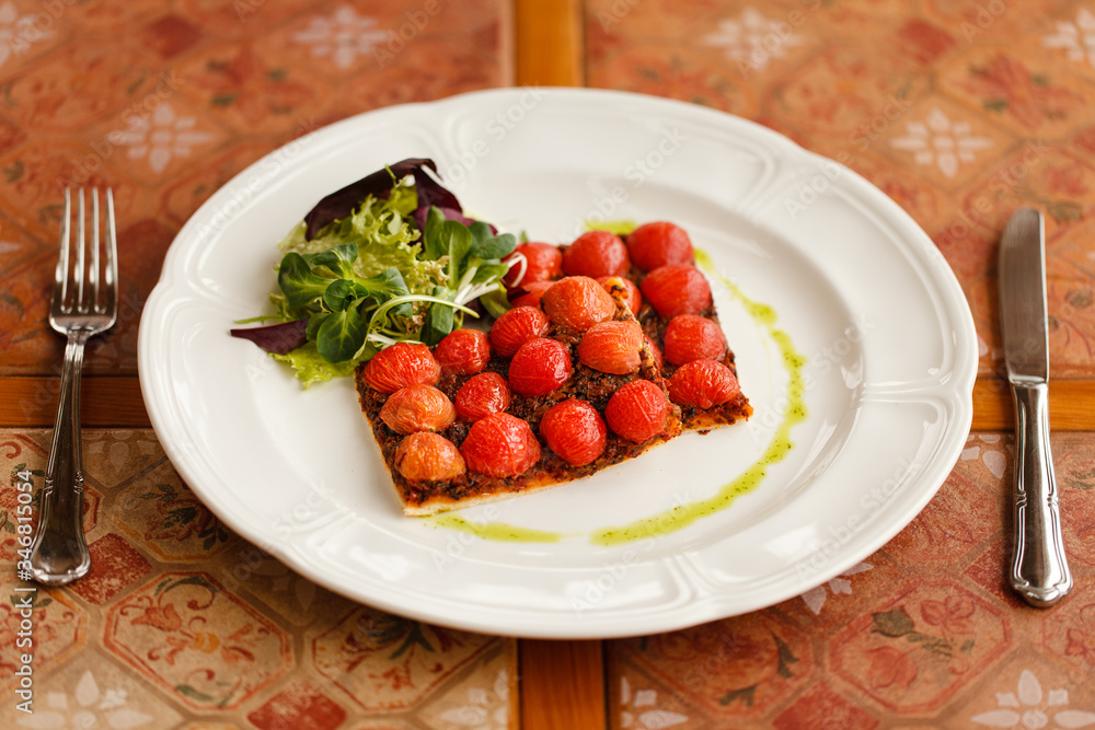 vegetarian pizza with cherry tomatoes, served with fresh herbs on a round white plate. on a wooden table top decorated with ceramic tiles vegetarian pizza with cherry tomatoes, served with fresh herbs on a round white plate. on a wooden table top decorated with ceramic tiles