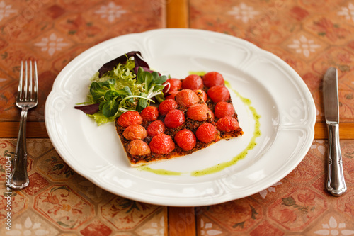 vegetarian pizza with cherry tomatoes, served with fresh herbs on a round white plate. on a wooden table top decorated with ceramic tiles