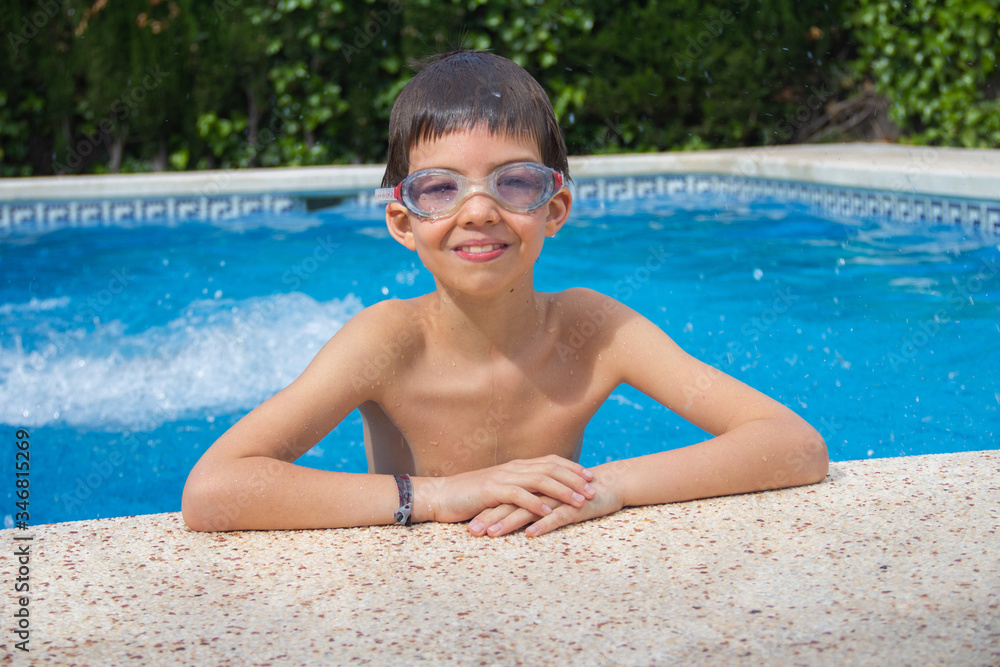 the boy crawled out of the pool with swimming goggles and smiling, against the background of a water splash summer, vacation, relax