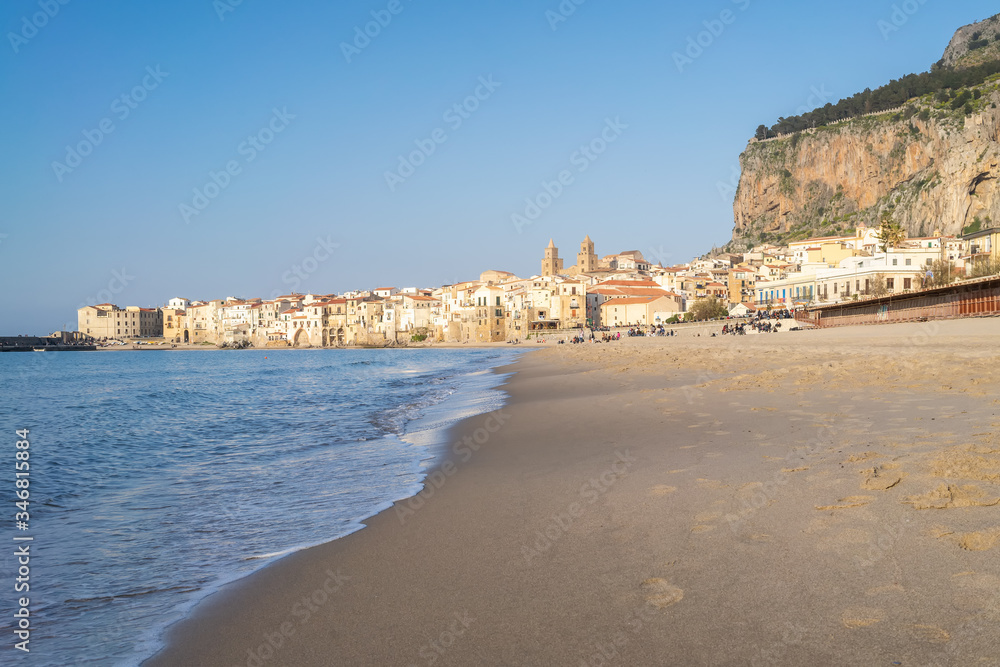 Idyllic view of Cefalu from the long sandy beach. Cathedral and Rocca di Cefalu rocky mountain on a sunny day in Cefalu, Sicily, Southern Italy.