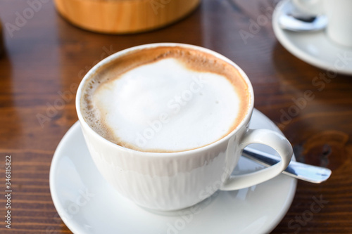 Simple coffee cup with milk foam on a white ceramic plate, on wooden background.