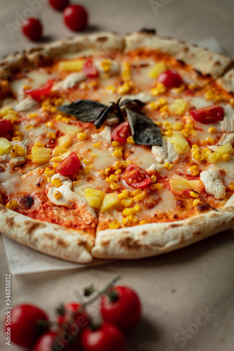 Pizza with chicken and pineapple, cheese, sauce and cherry tomatoes. The view from the top on the table and Kraft paper