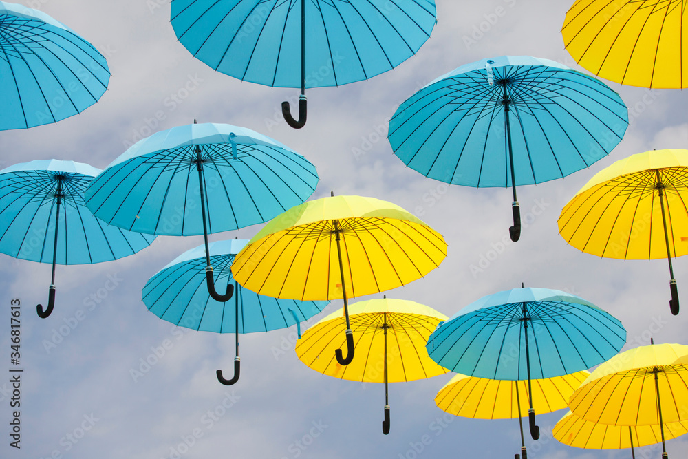 Yellow and blue umbrellas against a cloudy sky. Colorful umbrellas background. Colorful umbrellas in the sky. Street decoration.