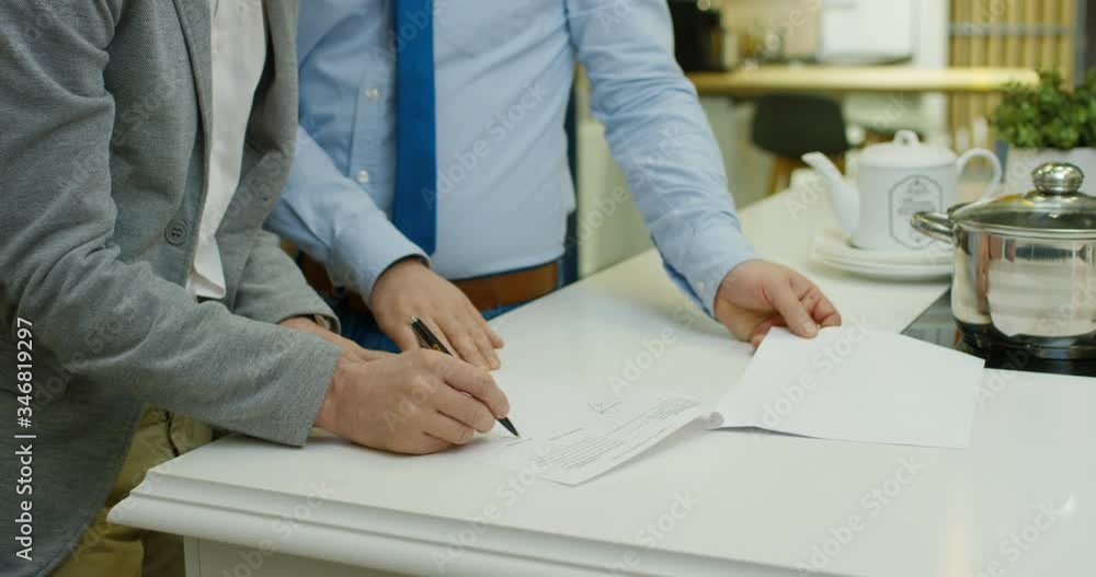 Close up of man buying house or apartment and signing document in kitchen on table. Male buyer sign contract. Mortgage treatment. Hypothec documents. Real estate agent deal.