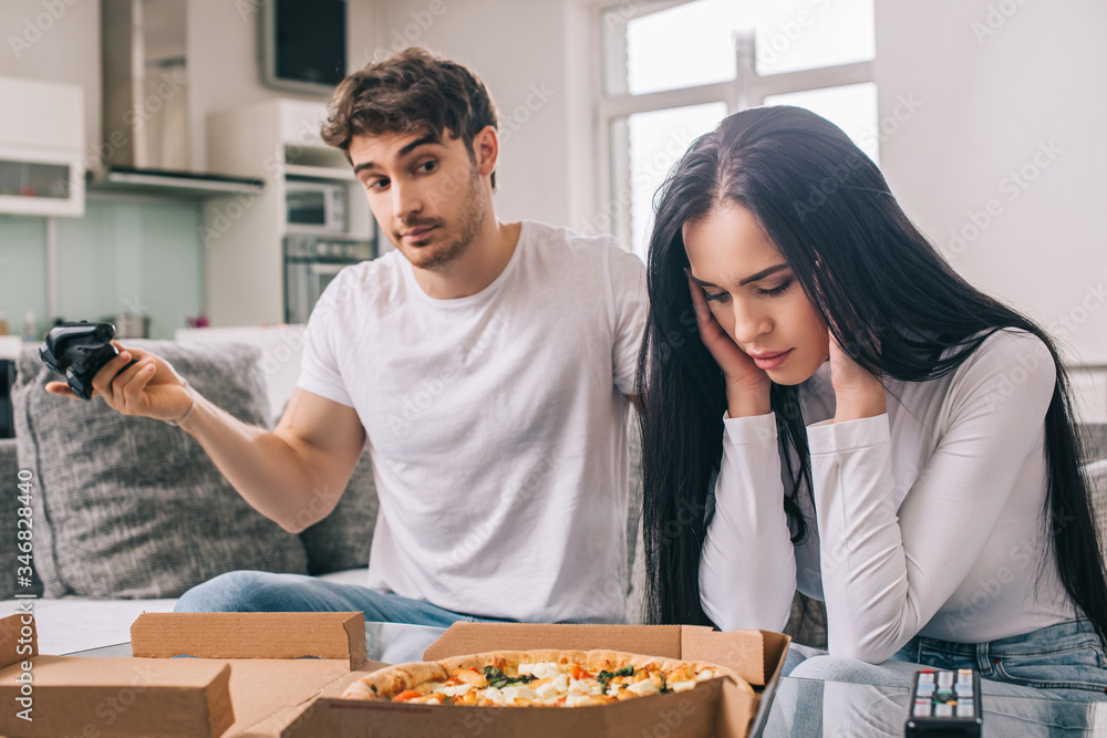 young sad couple with pizza and joystick quarreling during self isolation at home young sad couple with pizza and joystick quarreling during self isolation at home