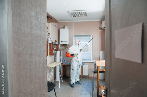 Coronavirus Pandemic. A disinfector in a protective suit and mask sprays disinfectants in house or office. Protection against COVID-19 disease. Prevention of spreding pneumonia virus with surfaces. photo