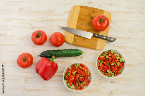 two white bowls with fresh salad of green cucumbers, red tomatoes and bell peppers on light wooden surface. Vegetables. Lowcalorie vitamin dietary food. Concept of healthy lifestyle