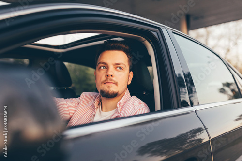 A young hansome driver sitting in a car and looking out the open window