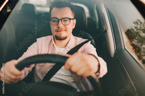 Windshield view of a car driver with seat belt. A young handsome man in glasses looking on the road