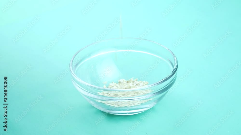 Pouring oatmeal into a glass bowl on a turquoise background Pouring oatmeal into a glass bowl on a turquoise background