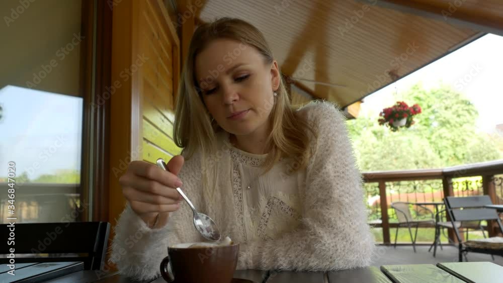 Beautiful young girl in white eats foam from coffee in a spoon in an outdoor cafe Beautiful young girl in white eats foam from coffee in a spoon in an outdoor cafe