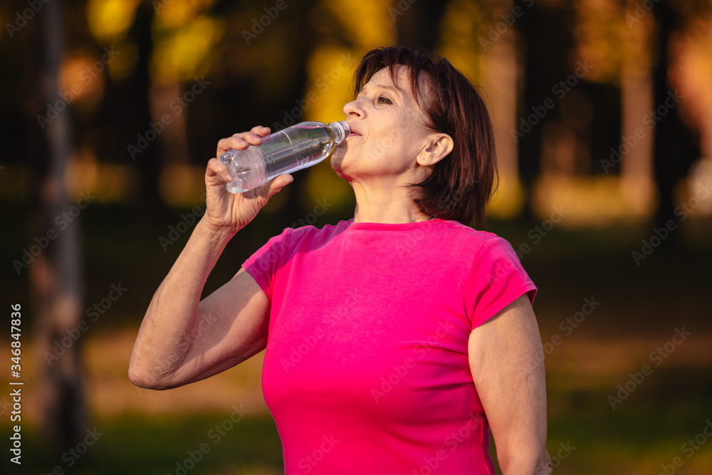 Elderly woman Drinking water from a bottle at sunset Elderly woman Drinking water from a bottle at sunset