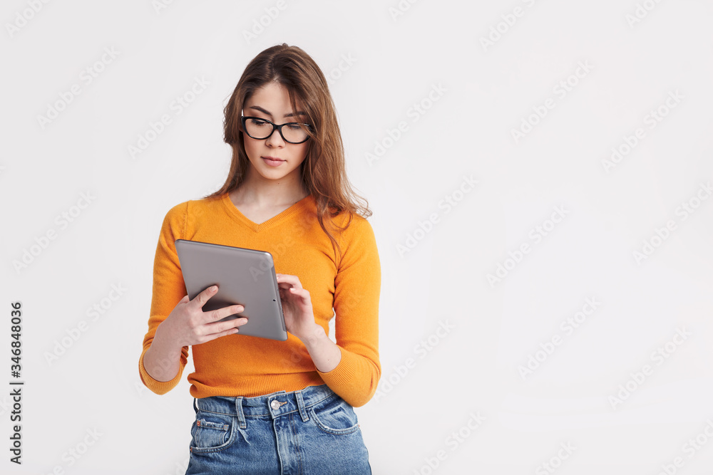 A beautiful young girl in glasses with a tablet in her hands poses on a light background. Education, distance learning. Space for text A beautiful young girl in glasses with a tablet in her hands poses on a light background. Education, distance learning. Space for text