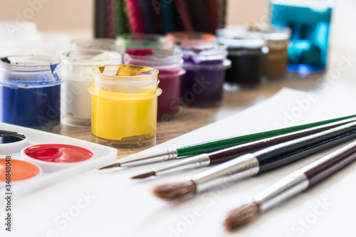 On the table are watercolor paints, brushes and gouache paints. Set for drawing, creativity and hobbies.