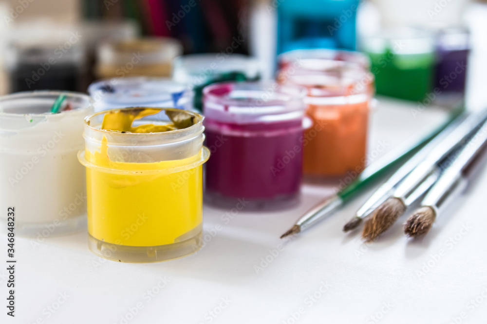 On the table are multi-colored gouache in a jar and brushes for painting. Set for drawing, creativity and hobbies.