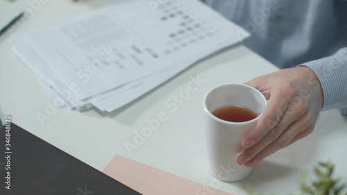 Office worker puts documents down and drinks tea