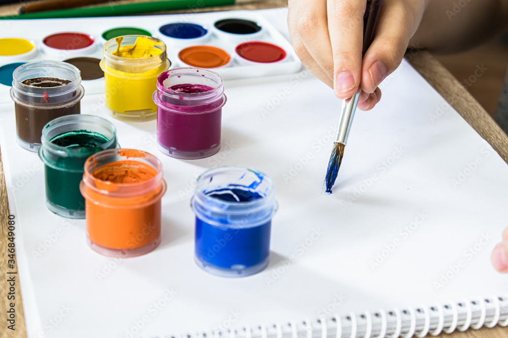 The child draws gouache on a white sheet and jars of paint are on the table. Hobbies and entertainment for children. The child draws gouache on a white sheet and jars of paint are on the table. Hobbies and entertainment for children.