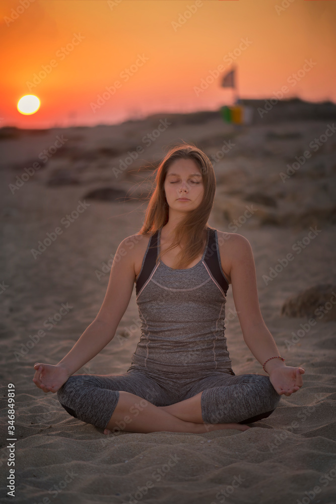 Young blond woman is meditating on a seaside in Healthy Pose on Beach in Sun Light Rays, Yoga Meditation practice concept