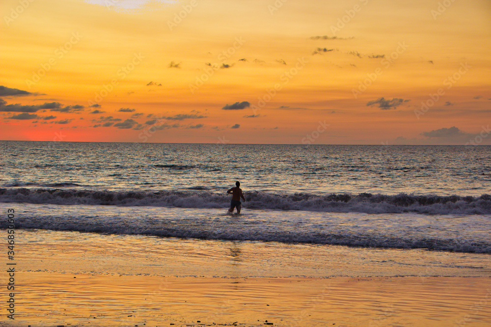 Hombre entrando al mar en un atardecer en una playa de Costa Rica
