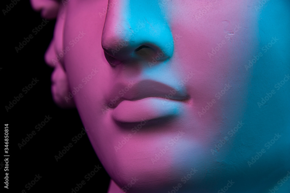 Colorful gypsum copy of ancient statue of human head for artists on a black background. Close up view lips. Plaster sculpture of human face. Toned blue and purple. Webpunk, surreal style poster. Colorful gypsum copy of ancient statue of human head for artists on a black background. Close up view lips. Plaster sculpture of human face. Toned blue and purple. Webpunk, surreal style poster.